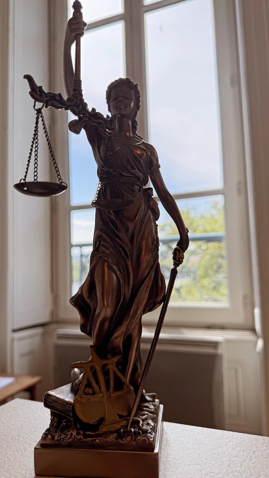 Statuette de la Justice tenant la balance, devant une fenêtre du cabinet